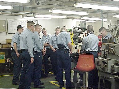 Cadet Machine shop: 1/c Cadet Glenn Milliken instructs underclass cadets in the finer points of the machine shop aboard Empire State